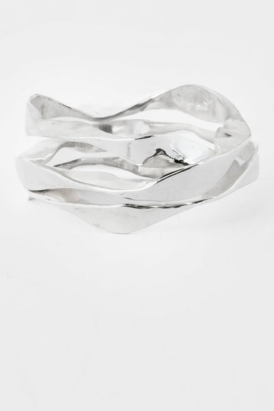 A polished silver ring with a fluid, wavy, overlapping design, photographed on a seamless light gray background.
